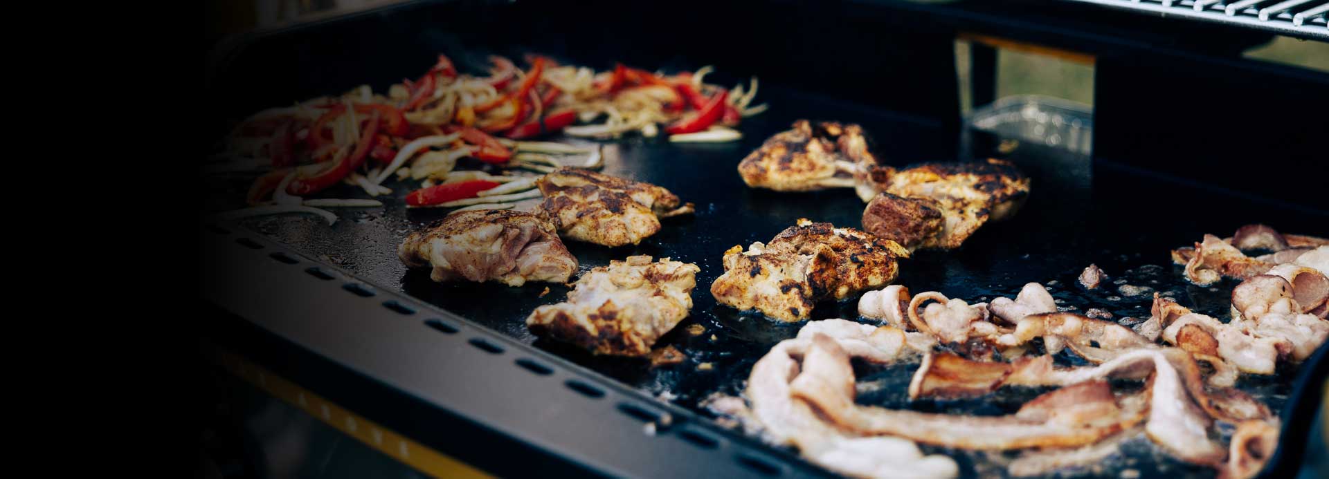 various BBQ food items cooking on a gas griddle